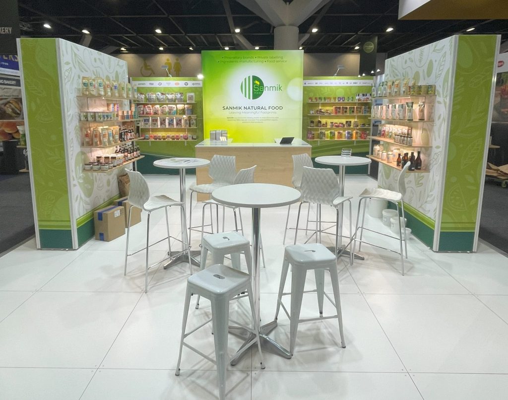 Custom exhibition stand for food industry expo. Large quantity of shelving for product display, cooking and sampling station. raised white floor, white high bars and stools. fabric digitally printed graphics.